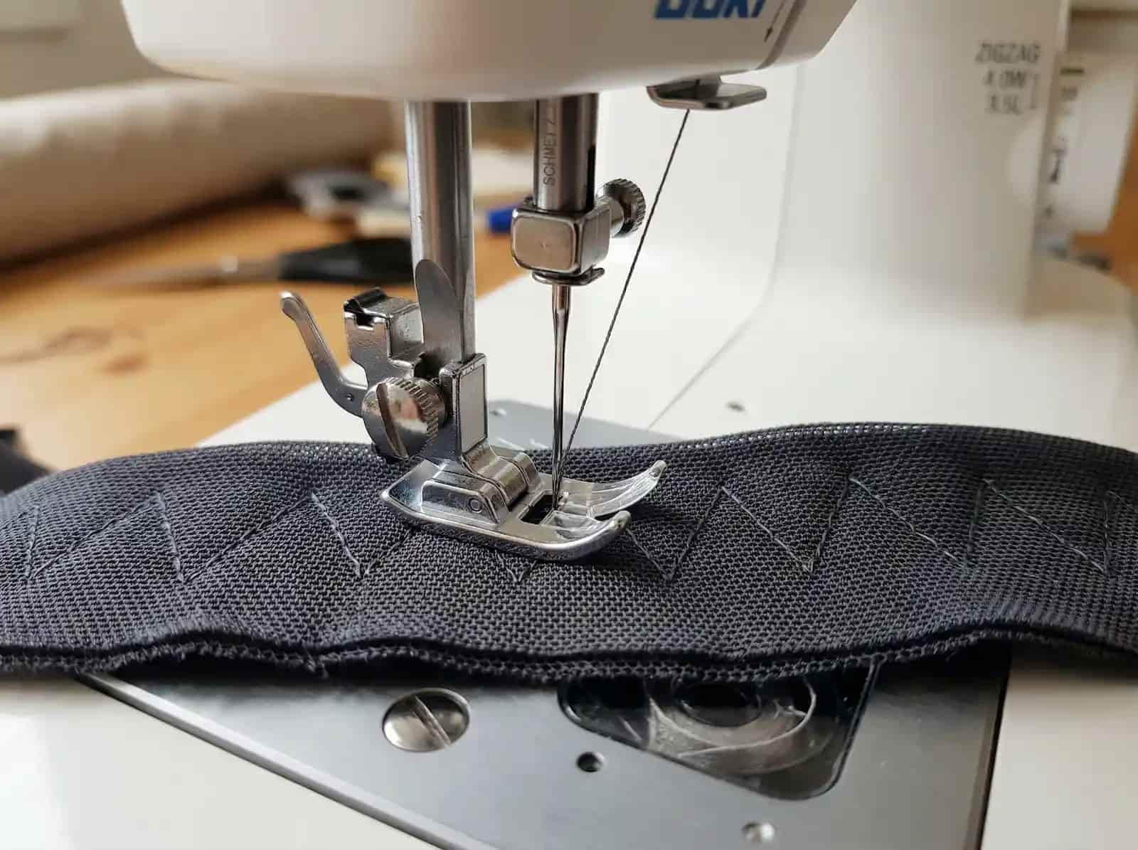 Zbliżenie na igłę maszyny do szycia mocującą haftki do paska biustonosza.