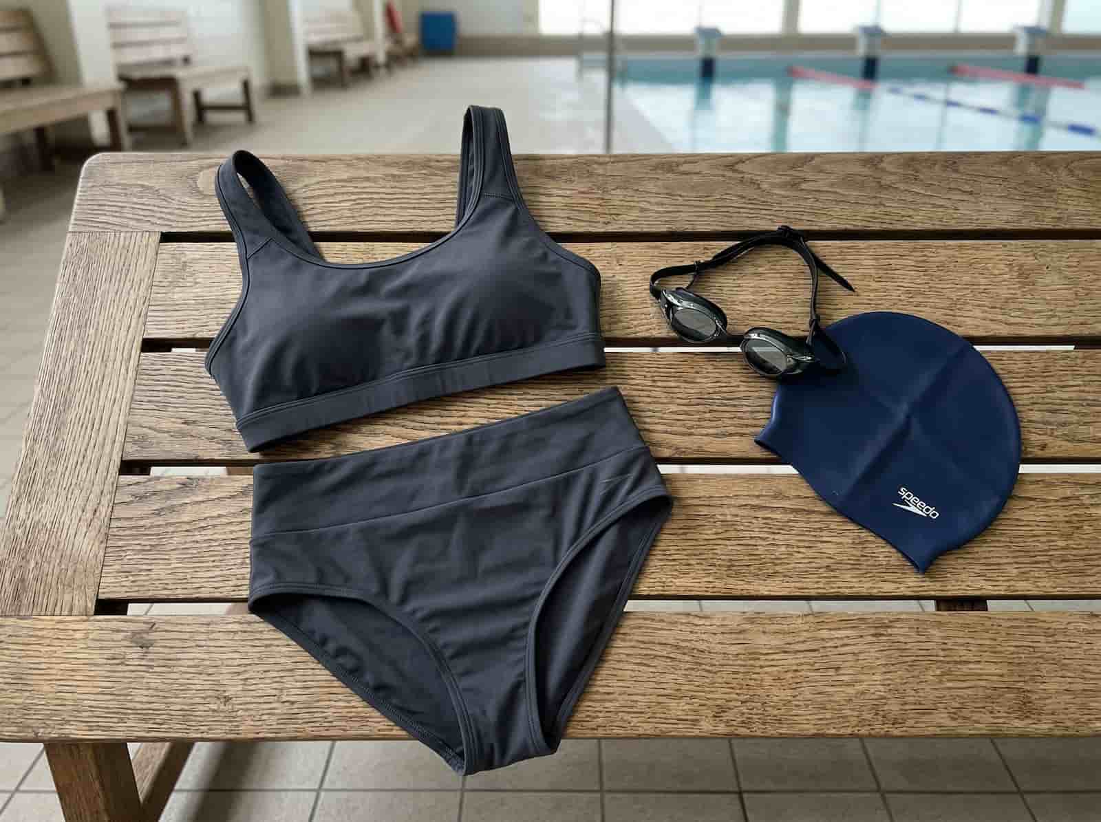 Sportowy dwuczęściowy strój kąpielowy z wysokim stanem leżący na ławce.